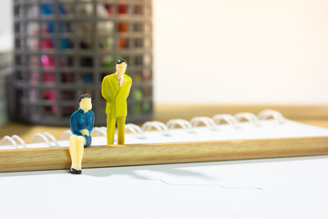 Miniature business man and women sitting on pencil with stationary background.