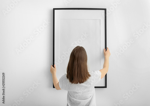 Cuadros en Lienzo Woman hanging blank photo frame on white wall