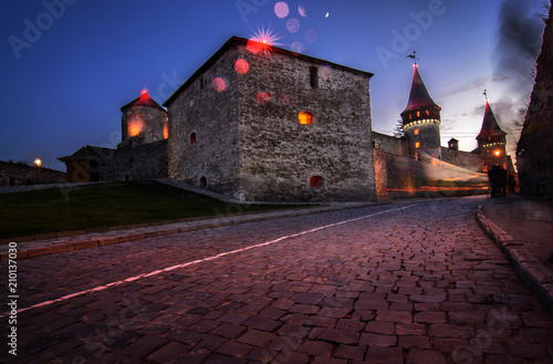 Plakat Krajobrazowa nocy fotografia forteca z światłami i zaludnia `sylwetki