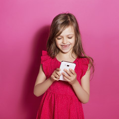 Little 8 years old girl make some emotional gesture with her hands on a pink neutral background. She has long brunette hair and wear red summer dress. Funny expression on her face