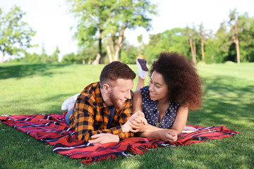 Wall Mural - Young loving interracial couple resting in park on spring day