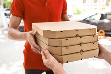 Young Man Giving Pizza Boxes To Woman Outdoors. Food Delivery Service