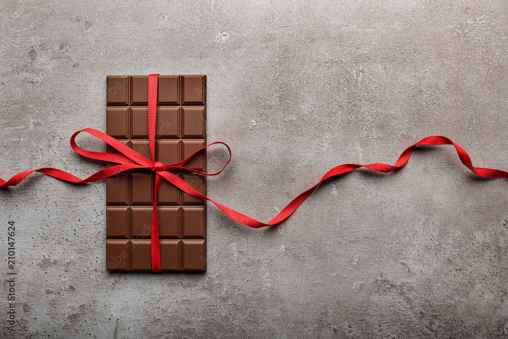 Tasty milk chocolate bar with ribbon on grey background