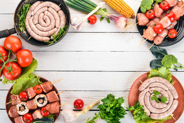 Assortment of meat for barbecue. Sausages, skewers and vegetables. On a wooden background. Top view. Copy space.