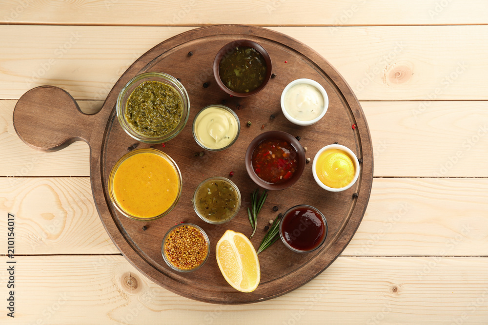 Bowls with different sauces on wooden board, top view