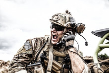 Special Forces Soldier, Military Communications Operator Or Maintainer In Helmet And Glasses, Screaming In Radio During Battle In Desert. Calling Up Reinforcements, Reporting Situation On Battlefield
