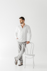 Wall Mural - handsome man in linen clothes standing near chair isolated on grey background