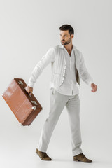 Wall Mural - stylish male tourist in linen clothes carrying vintage suitcase isolated on grey background