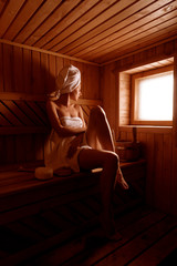 Wall Mural - girl in a spa treatment in a traditional sauna with a brush for skin and a washcloth. relaxes wrapped in a white towel