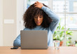 © Krakenimages.com - African american woman using laptop computer at home stressed with hand on head, shocked with shame and surprise face, angry and frustrated. Fear and upset for mistake.
