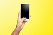© Mayatnikstudio - Mockup of female hand holding frameless cell phone with black screen isolated at yellow background.