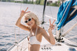 smiling young woman in sunglasses and swimwear doing peace signs on yacht