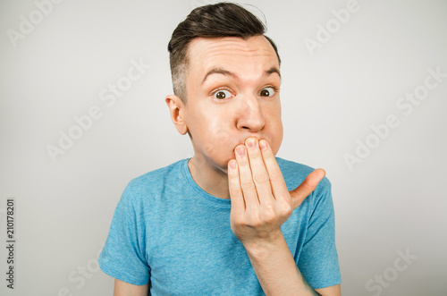Fotomural Young guy dressed in a blue t-shirt closing mouth from vomiting on a light background