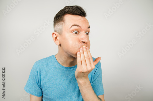 Fotografía Young guy dressed in a blue t-shirt closing mouth from vomiting on a light background