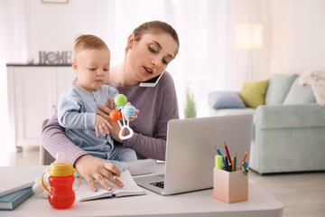 Wall Mural - Young mother with baby talking on phone while working at home