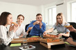 © Pixel-Shot - Young people eating pizza at table in office