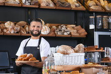 Male Baker Holding Wooden Board With Delicious Croissants In Shop