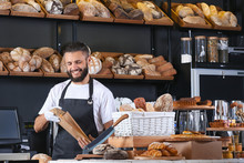 Young Man Packaging Bread For Customer In Bakery