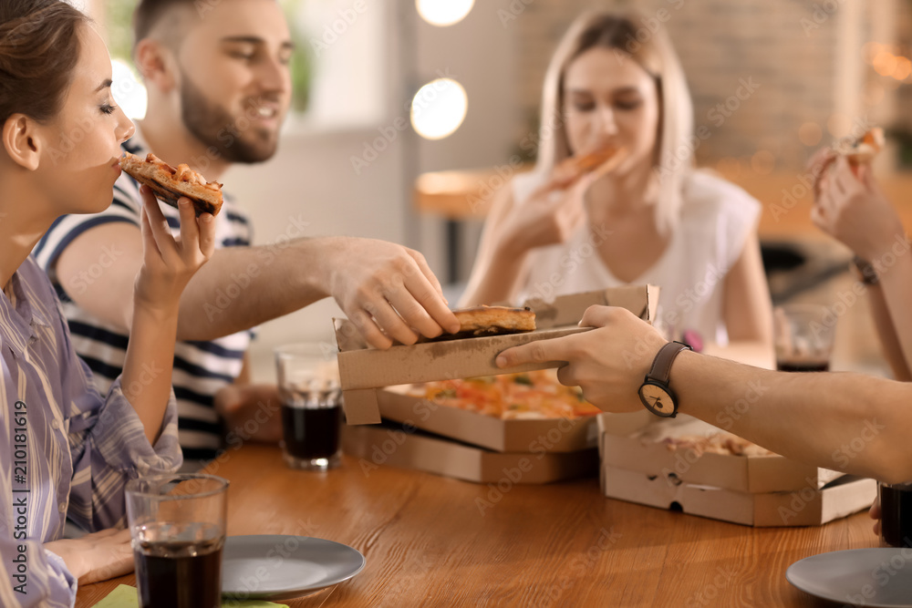 Young people eating pizza at table indoors