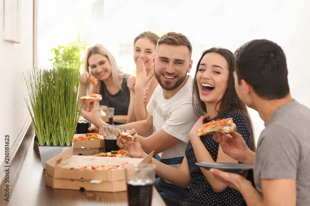Young people eating pizza at table indoors