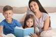 © Pixel-Shot - Mother and her children reading book together at home