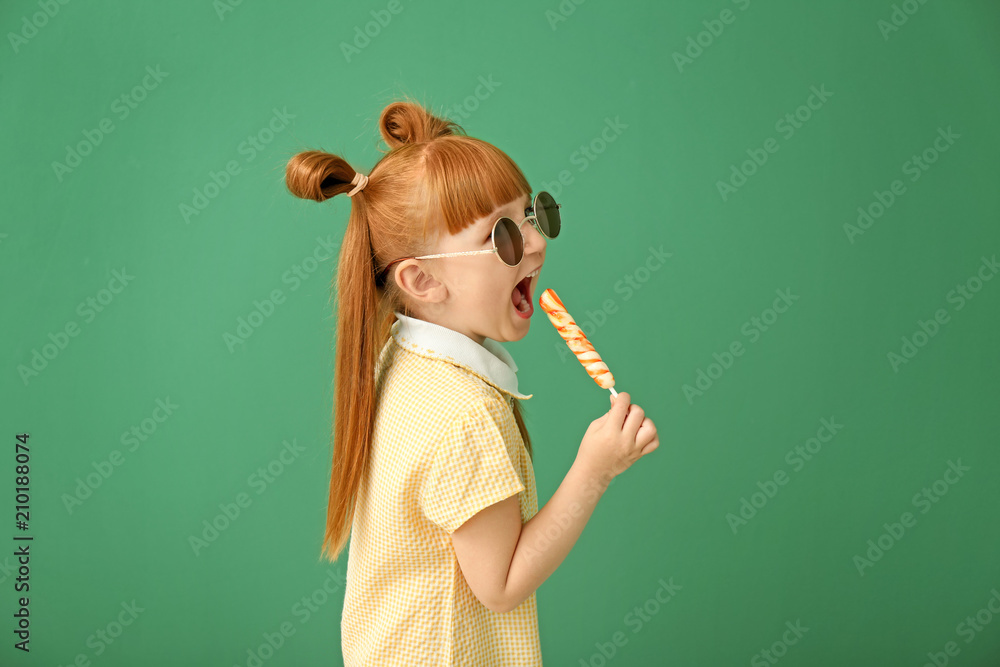 Cute little girl with lollipop on color background