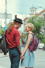 happy stylish couple of tourists with backpacks holding hands in city