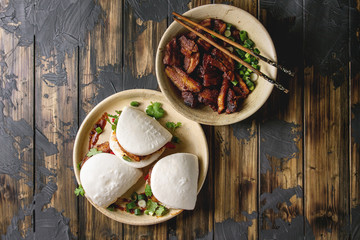 Wall Mural - Asian sandwich steamed gua bao buns with pork belly, greens and vegetables served in ceramic plate over dark wooden plank background. Asian style fast food dinner. Flat lay, space