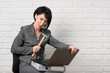 © soleg - angry business woman with laptop and folders having stress, dressed in a gray suit poses in front of a white wall