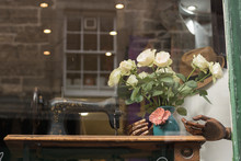 Showcase In An Old Vintage Style. An Old Sewing Machine, A Vase, Roses, A Wooden Mannequin's Hand, A Hat Is Outside The Window. It`s Stylish Old Stuff On A Fashion Street. 