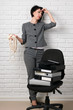 © soleg - angry business woman with laptop and folders having stress, dressed in a gray suit poses in front of a white wall