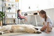 © LIGHTFIELD STUDIOS - selective focus of kid playing with golden retriever dog on floor while sister using laptop at home