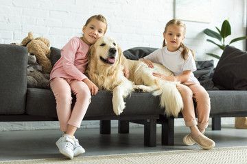 Wall Mural - adorable kids hugging golden retriever dog while sitting on sofa at home