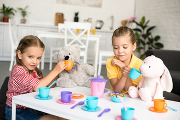 adorable little sisters pretending to have tea party together at home