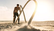 © Jacob Lund - Man doing workout using battling ropes at the beach