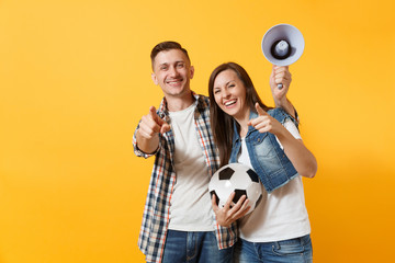 Young happy cheerful couple supporter, woman man, football fans cheer up support team, holding megaphone, soccer ball isolated on yellow background. Sport, family leisure, people lifestyle concept.