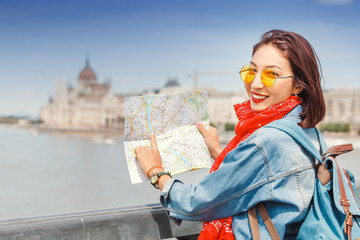 Wall Mural - Happy asian hipster woman tourist with map travels in Budapest at Hungarian Parliament at the background