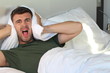 Frustrated man covering his ears with pillow