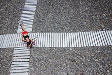 Overhead Woman Lying On A Cross Road Of Two White Wooden Path Ways On Pebble Beach.