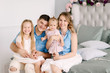 © oes - Family portrait. Young parents Mom and Dad are sitting with two lovely daughters on the bed in a large bright room. Parents hug their children and they are happy