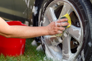 Men's hands are cleaning wheels with a sponge and foam.