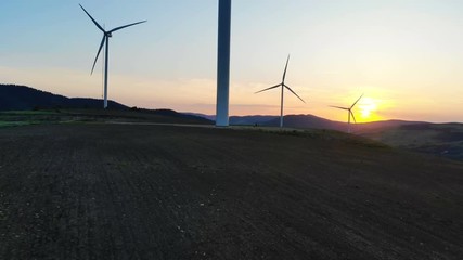 Wall Mural - scenic sunset over mountains with the silhouettes of wind turbines blades rotating converting kinetic energy into electricity aerial shooting bright sunlight rising ecology life idyll peaceful horizon