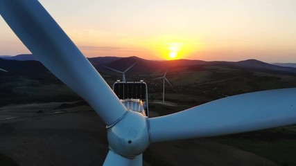 Wall Mural - closeup aerial view of rotating blades of wind turbine with scenic colorful sunset over the mountains on background agricultural fields on hillside eco farm modern eceltric station renewable energy