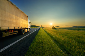 Wall Mural - truck driving on the asphalt road in a rural landscape in the golden sunset