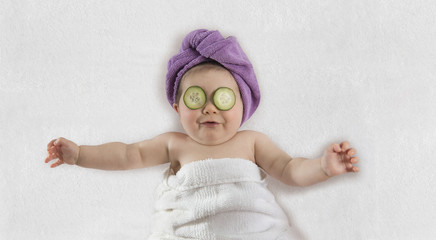 funny baby girl wrapped in white towel with cucumbers on her eyes