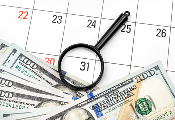 Magnifying glass with money on calendar. Focus on last day of month. Business concept.