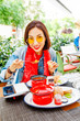 Young beautiful asian girl eating hungarian goulash soup from a decorative red casserole in outdoor restaurant