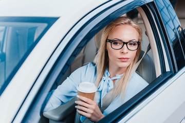 portrait of blonde businesswoman with coffee to go driving car