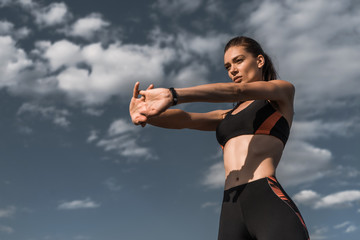 Wall Mural - attractive sportswoman stretching hands against blue cloudy sky