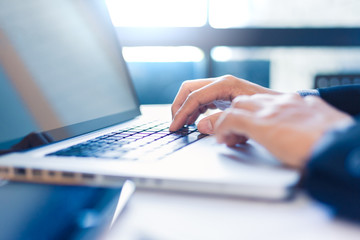 Businessman hands working on laptop computer in his office by a bright window
